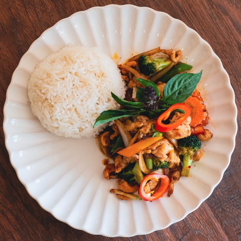 Chicken stir-fry with broccoli, carrots, and cashews, served with white rice on a scalloped plate.