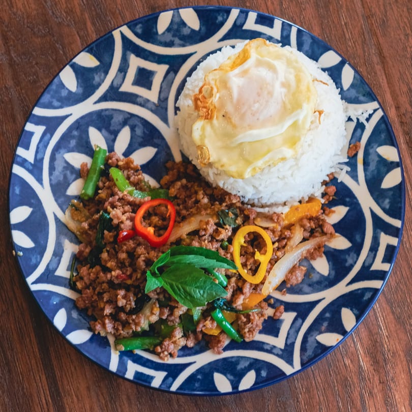 Thai basil pork with rice and a fried egg on a blue and white patterned plate.