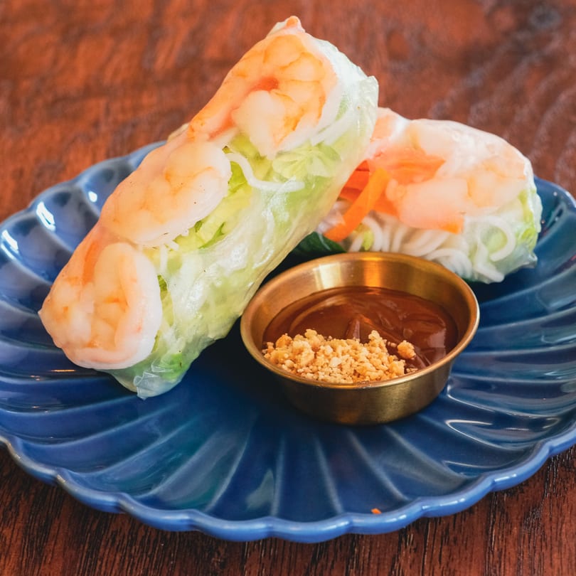 Two fresh shrimp spring rolls with lettuce, noodles, and carrots, served with peanut sauce.
