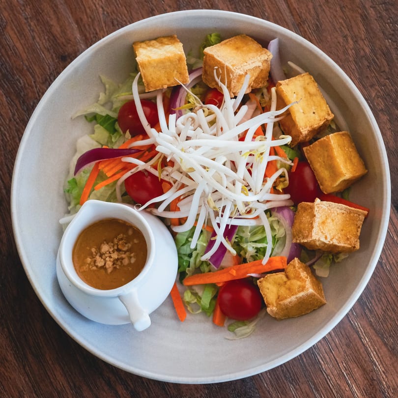 A vibrant salad with fried tofu, bean sprouts, lettuce, tomatoes, and a side of peanut dressing.