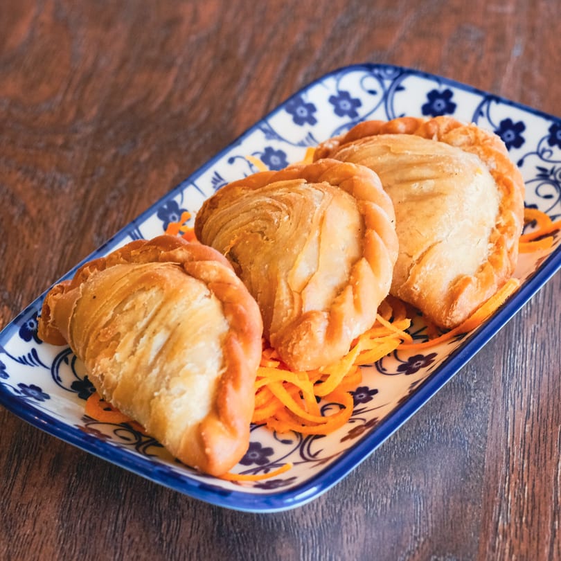 Three golden-brown curry puffs with crimped edges, served on a blue and white patterned plate.
