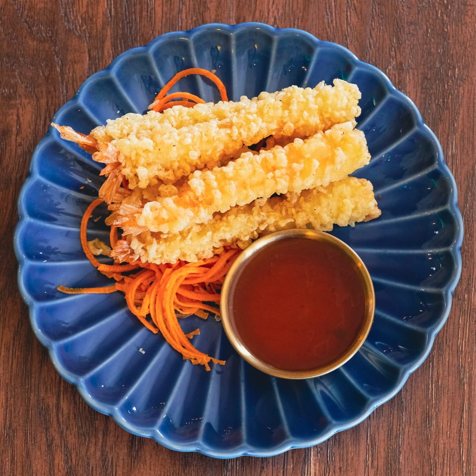 Crispy fried shrimp tempura with shredded carrots and a side of dipping sauce on a blue plate.