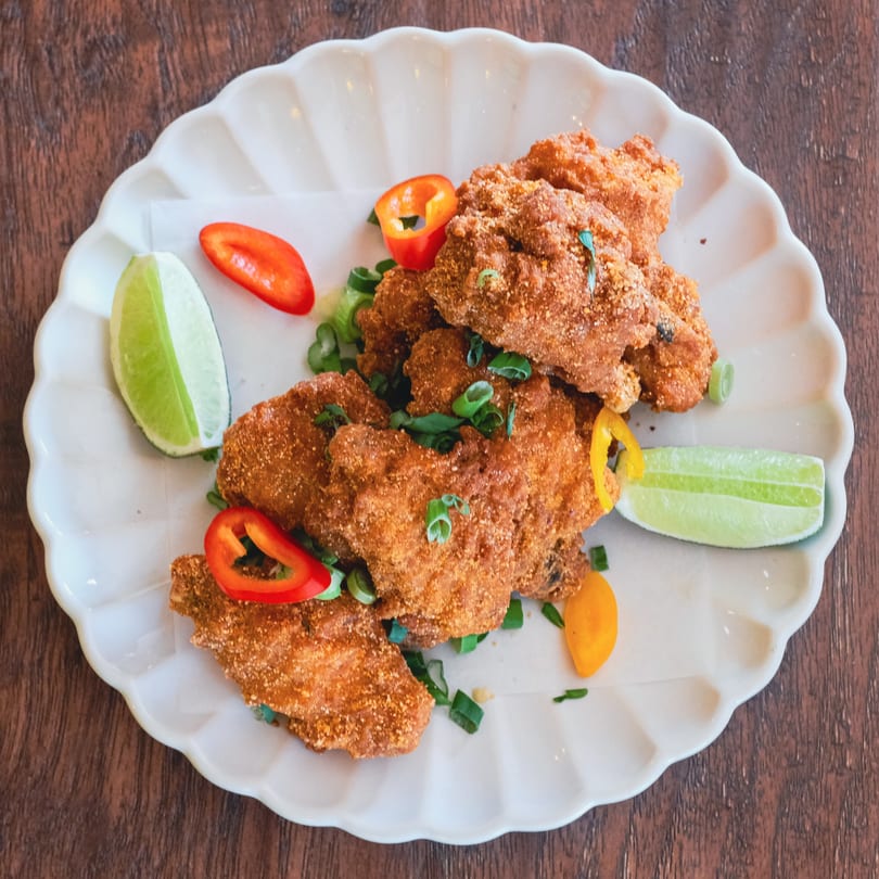 Crispy fried chicken pieces garnished with chopped scallions, red and yellow bell peppers, and lime wedges.