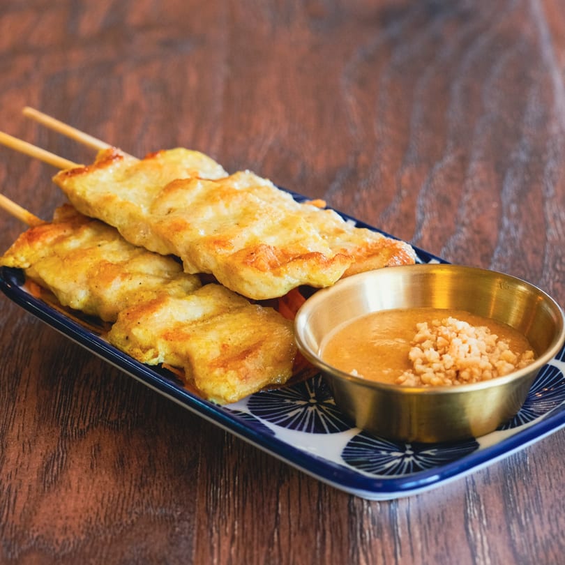 Chicken satay skewers with peanut sauce, garnished with crushed peanuts, on a patterned plate.